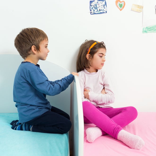 Brother and sister sit on beds in shared bedroom