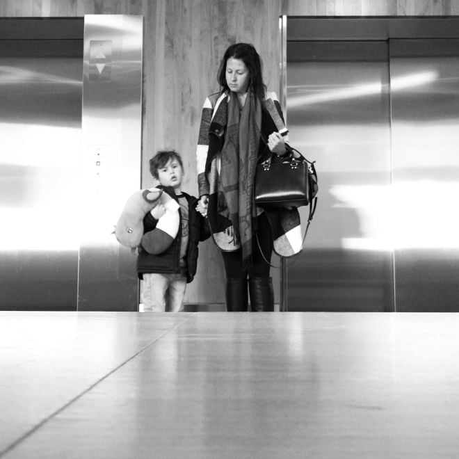 A woman holding a boy's hand in front of elevators.