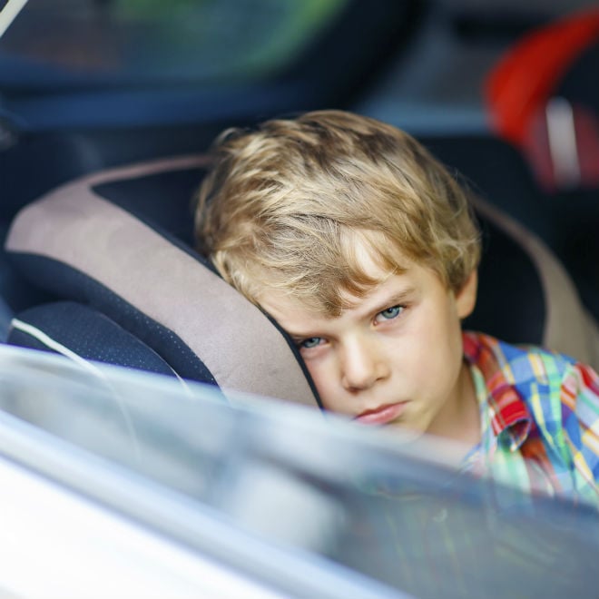 Kid looking sick and tired in the back of a car