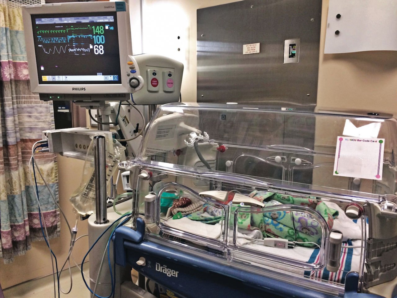 Baby in an incubator with attached monitors and displays in the NICU