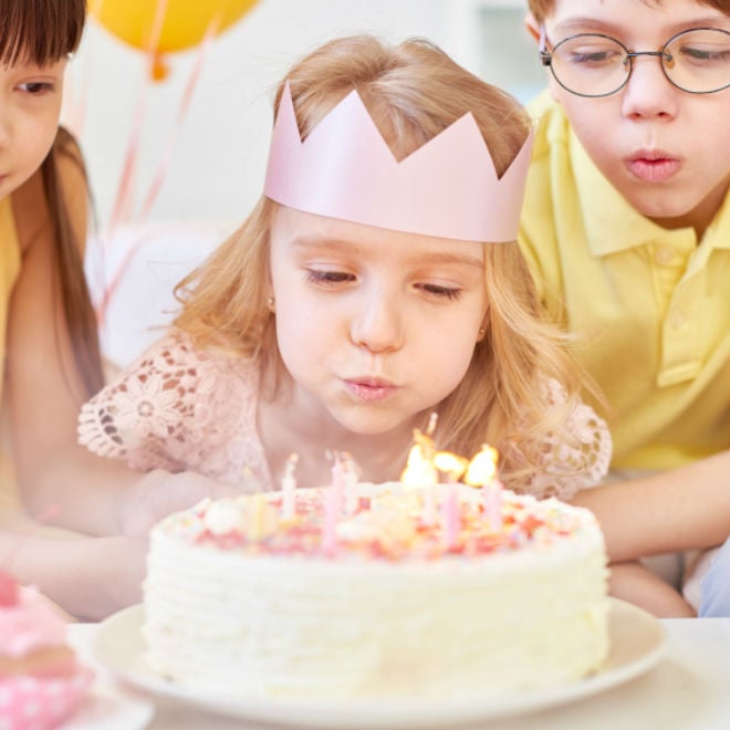 little girl blowing out candles on a cake at a home birthday party