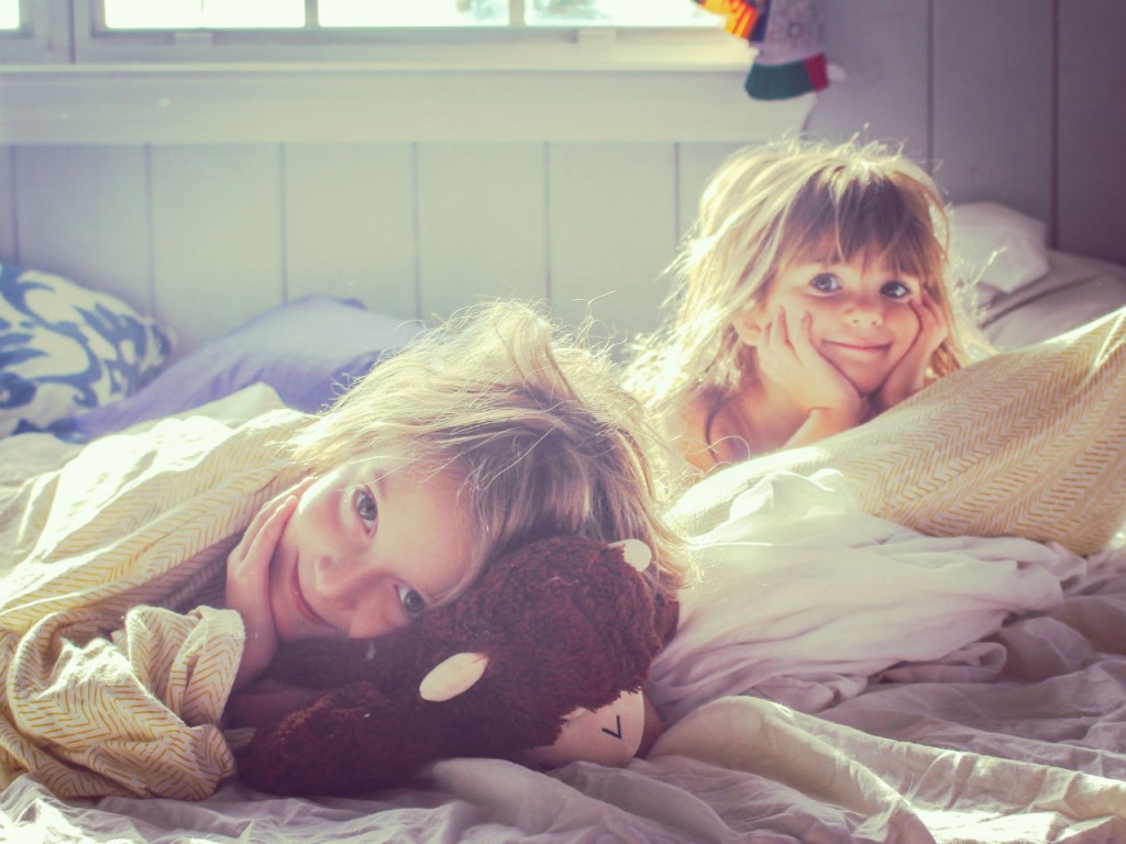 Two young girls lie in bed and stare at the camera