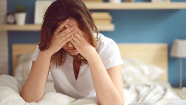 Woman on bed with her head in her hands worrying about premature menopause