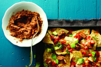 bowl of refried beans and nachos with cheese, tomatoes and avocado