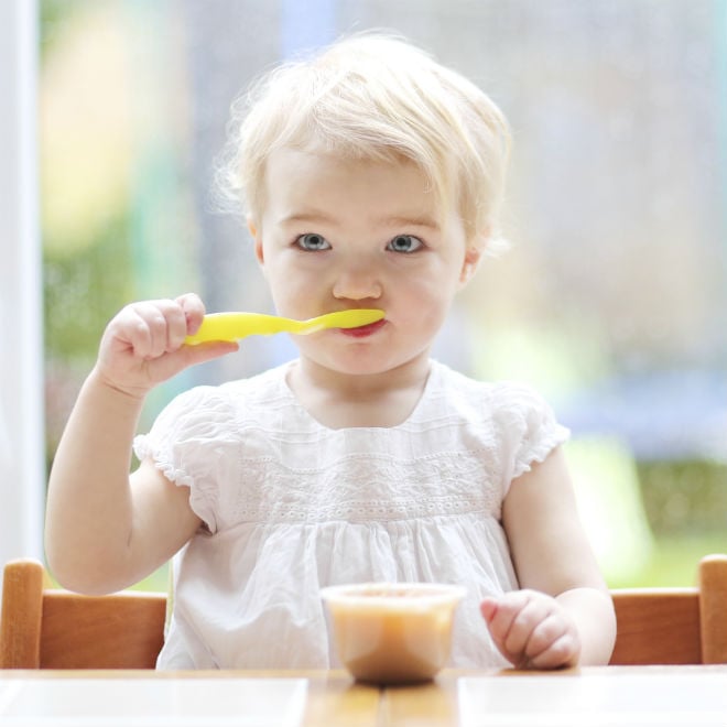 weaning toddler with a spoon in her mouth