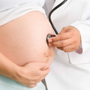 doctor pressing a stethoscope to a pregnant woman's belly
