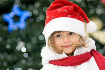 a little girl wearing a santa costume smiles in front of christmas decorations