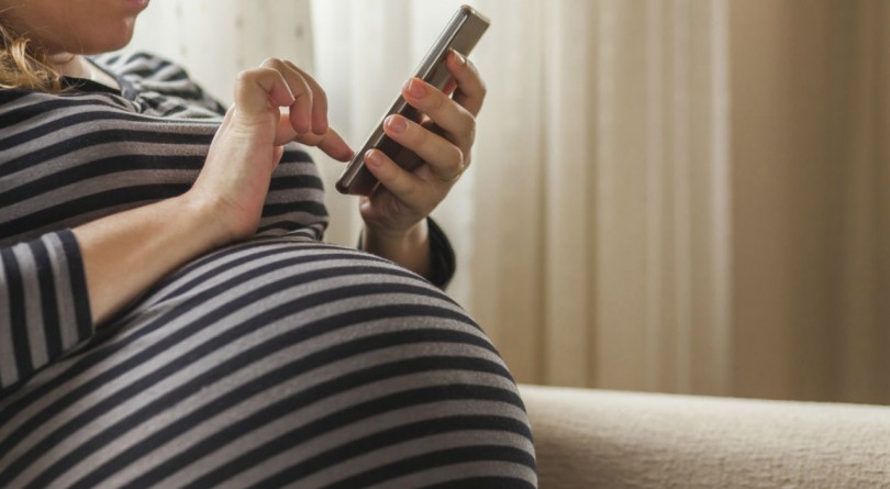 Pregnant woman sitting on the couch looking at her phone, belly in foreground