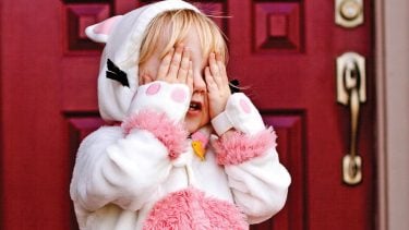 A kid in a cat costume covering her eyes