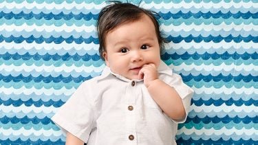 5 month old baby in a white button up and putting one finger in his mouth