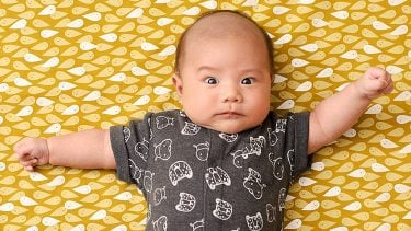 five week old baby laying against yellow background