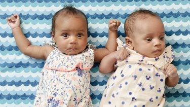 2 seven week old babies with arms up and laying against blue background