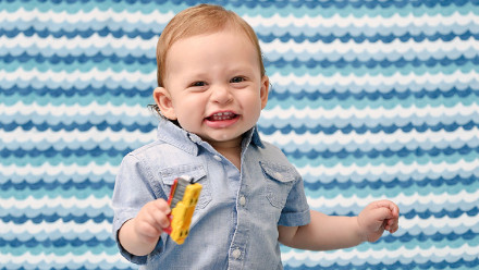 1 year old toddler holding a toy and smiling