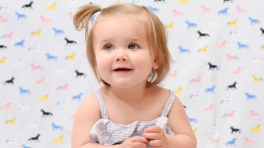 14 month old girl with a ponytail looking up and smiling