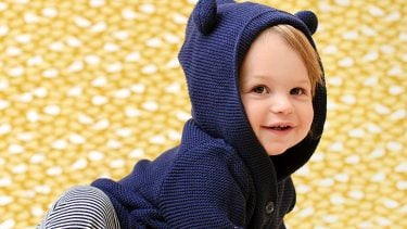 17 month old smiling in a cute blue sweater with blue horns on hood