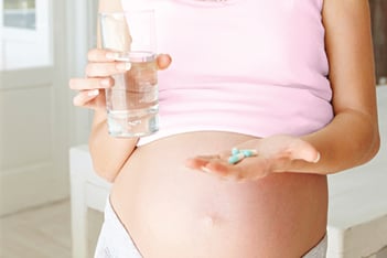 pregnant woman holds a glass of water and some meds