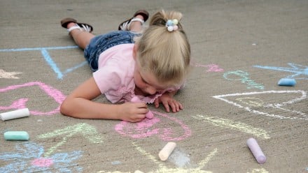 Little girl lying on pavement while drawing with chalk
