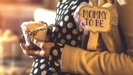 A pregnant woman holding a cupcake and a sign saying Mom to be