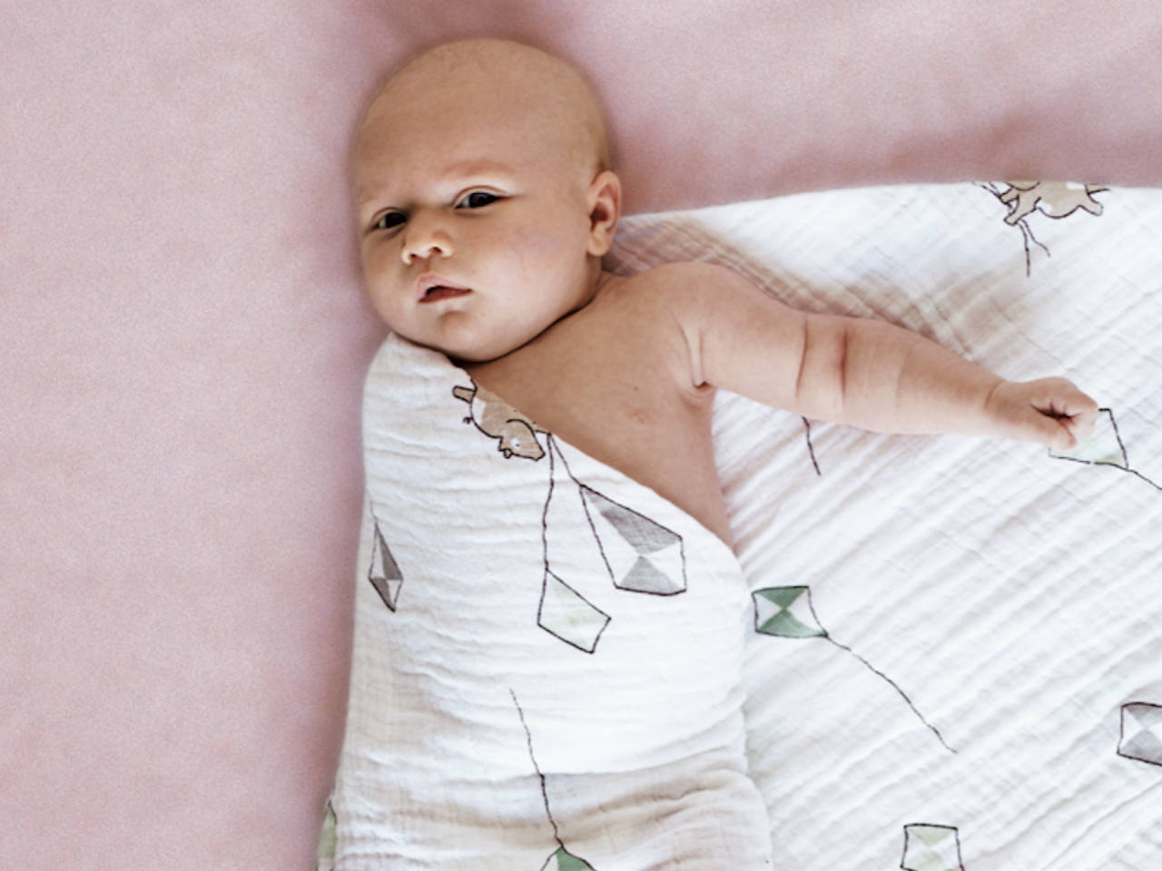 A baby half swaddled in a muslin blanket