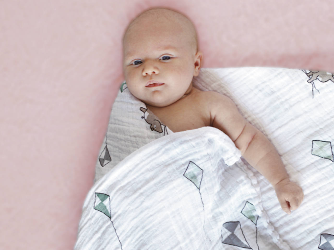 A baby being swaddled in a muslin blanket