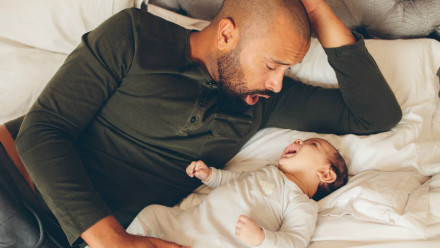 A dad making faces at a baby on the bed