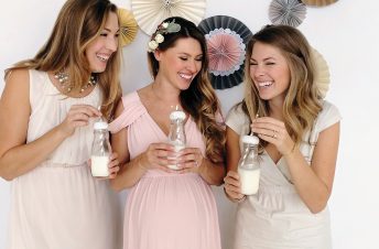 Three women playing a baby shower game with baby bottles