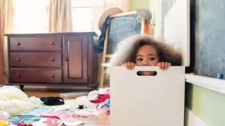 A little girl hiding in a box in her messy room