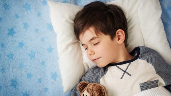 Preschool boy sleeping in bed with blue sheets with a teddy bear