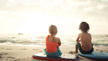 Two kids sitting on boogie boards on the beach