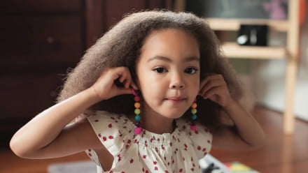 A little girl holding pompom earrings up to her ears