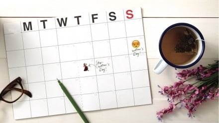 A white calendar surrounded by flowers and a mug of tea