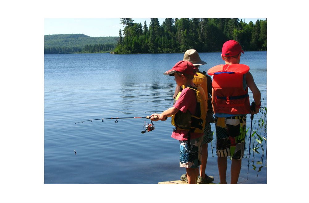 three boys in lifejackets fishing off a dock in summertime