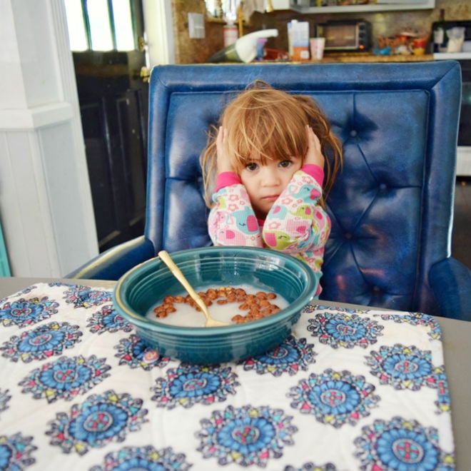 A little girl sits in front of a bowl of cereal with her ears covered