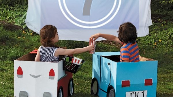 Two kids sitting in cardboard cars for an outdoor movie