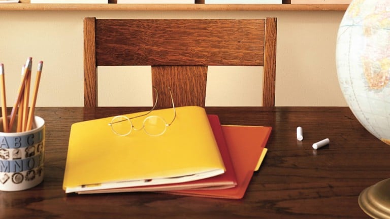 A classroom with a teacher's desk with folders on it