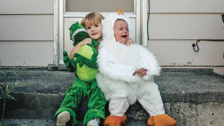 Two kids in costumes sitting on the porch, with one of them crying