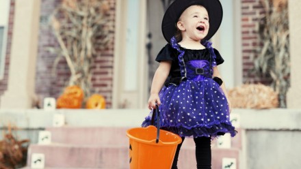 A little girl dressed as a witch standing on a doorstep on Halloween
