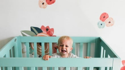 A baby crying in her turquoise crib