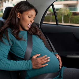 Pregnant woman sits in backseat of car showing signs of labour