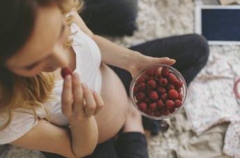 A pregnant woman sitting on the bed eating a bowl of raspberries