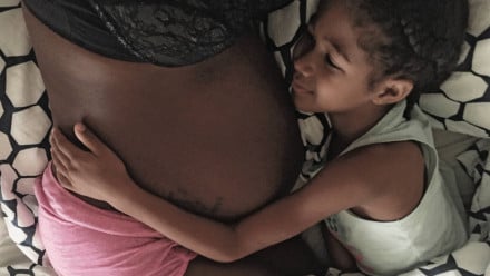 A young girl hugging a woman's pregnant belly