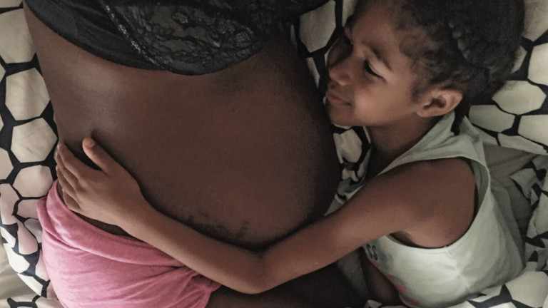 A young girl hugging a woman's pregnant belly
