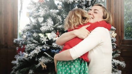 A little girl hugging a woman in front of a christmas tree