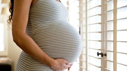 Pregnant woman standing at a window holding her belly