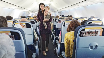 A woman with her toddler in her arms walking down a plane aisle