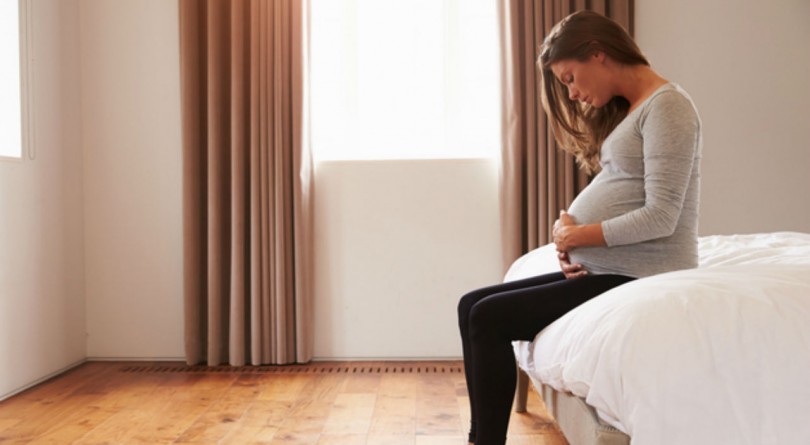 Pregnant woman sitting on bed holding tummy