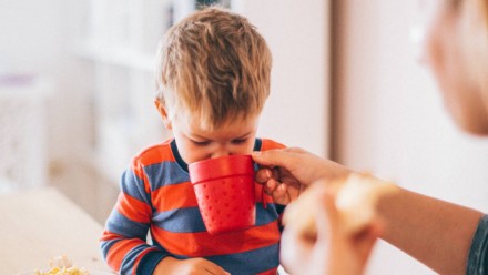 A woman helping a little boy drink from a mug