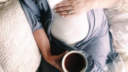 A pregnant woman sitting in bed and holding a cup of tea