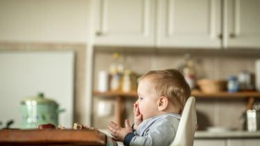 baby sits in a high chair in the kitchen eating
