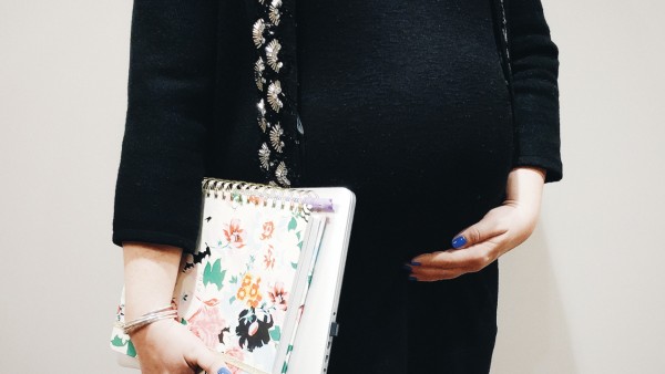 pregnant woman holds belly while holding notebooks